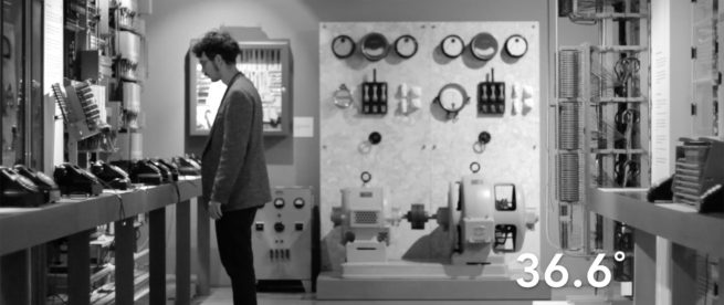 Still from the film 36,6 degree. it Depicts the performer standing in front of many old analog telephones.