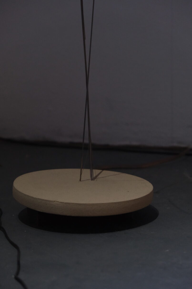 detail of the installation showing a metal rod swiping a ceramic surface.