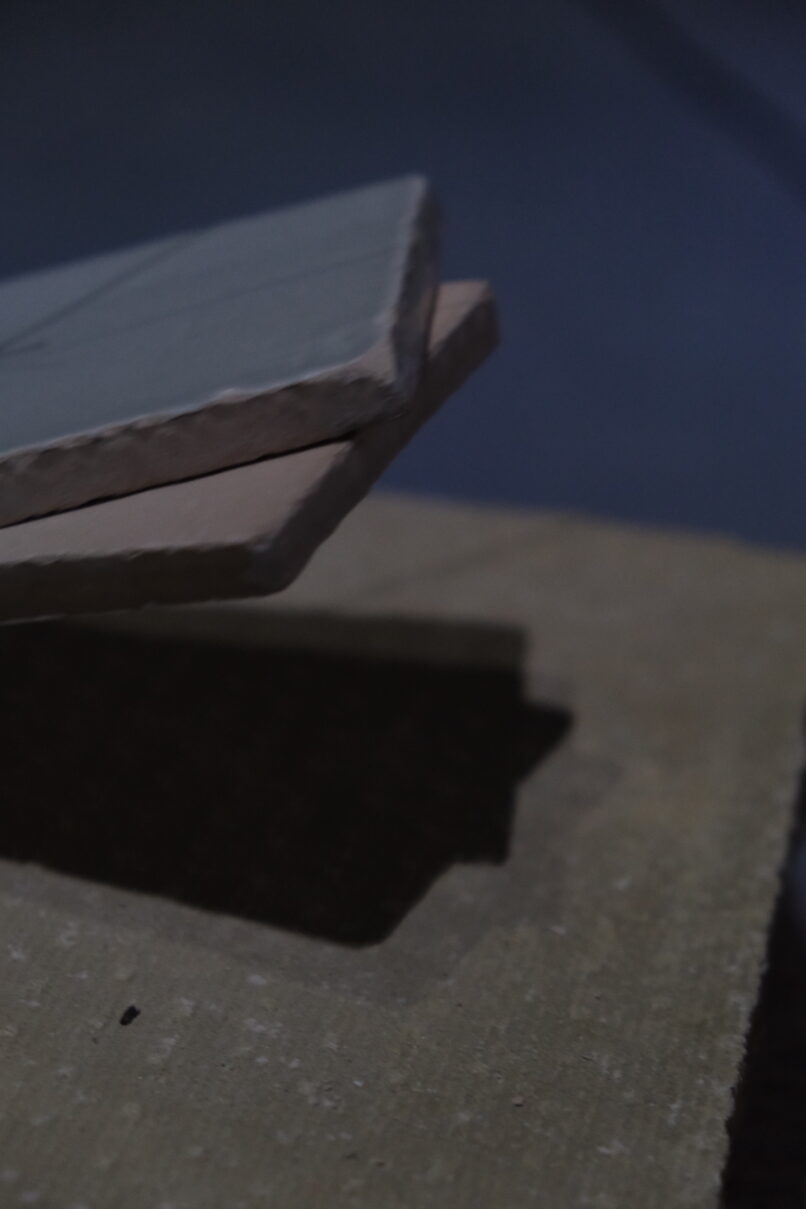 Detail of the installation showing two ceiling suspended tiles hitting a brick on the floor