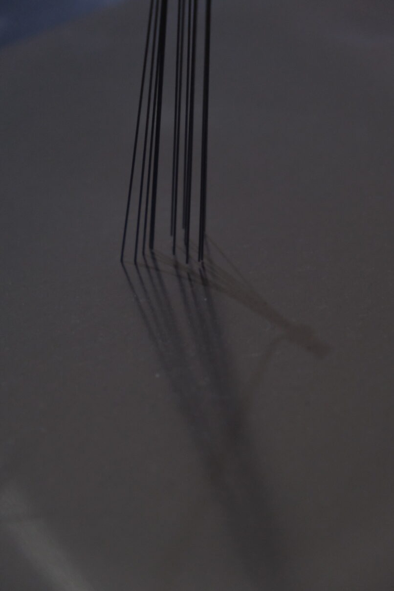 detail of the art installation showing thin metal rods swiping an aluminum surface.